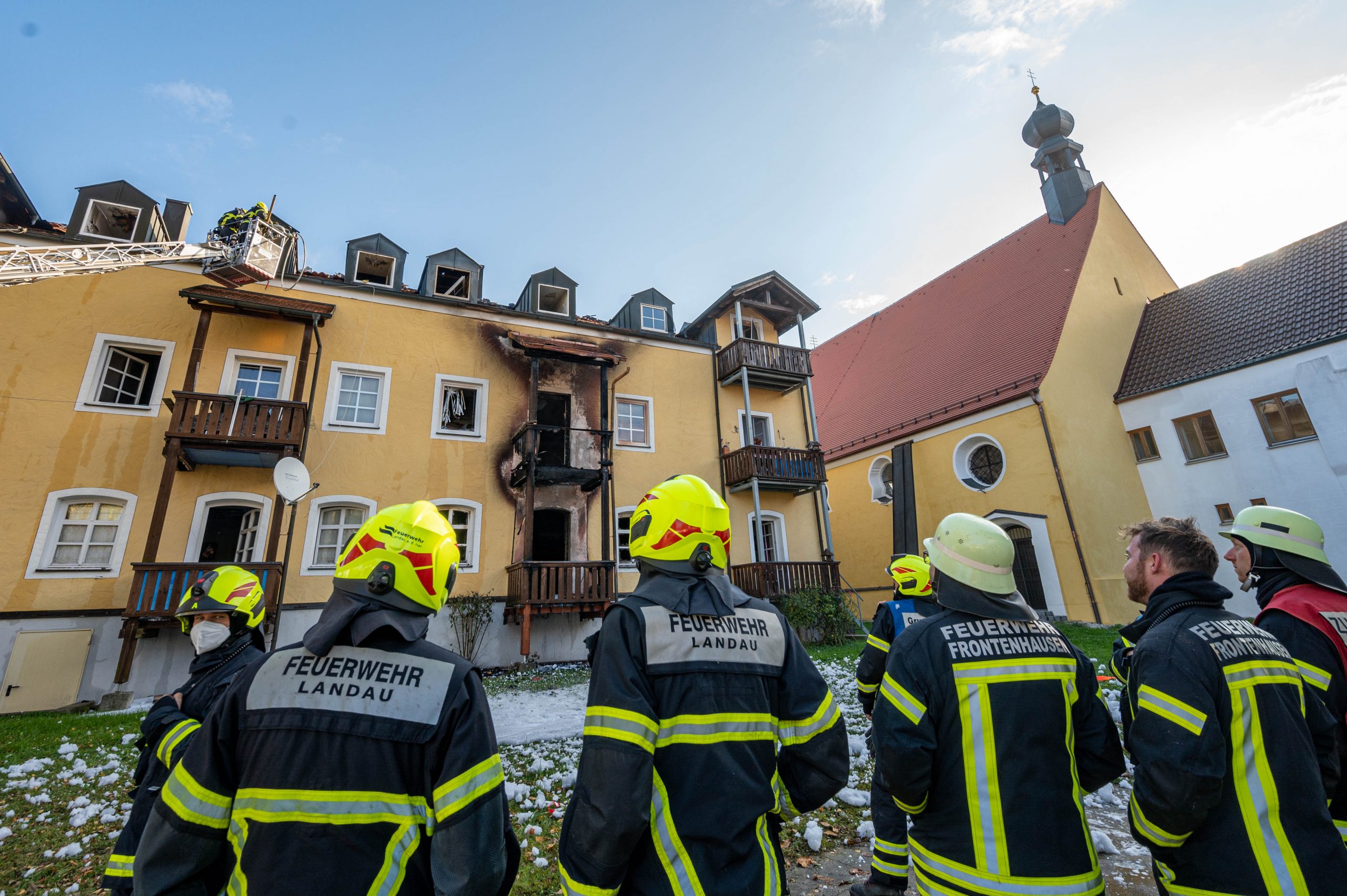 Feuerwehrmänner stehen vor dem ausgebrannten Mehrfamilienhaus in Reisbach.