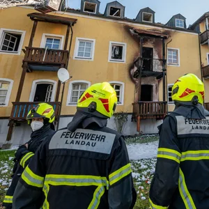 Feuerwehrmänner stehen vor dem ausgebrannten Mehrfamilienhaus in Reisbach.