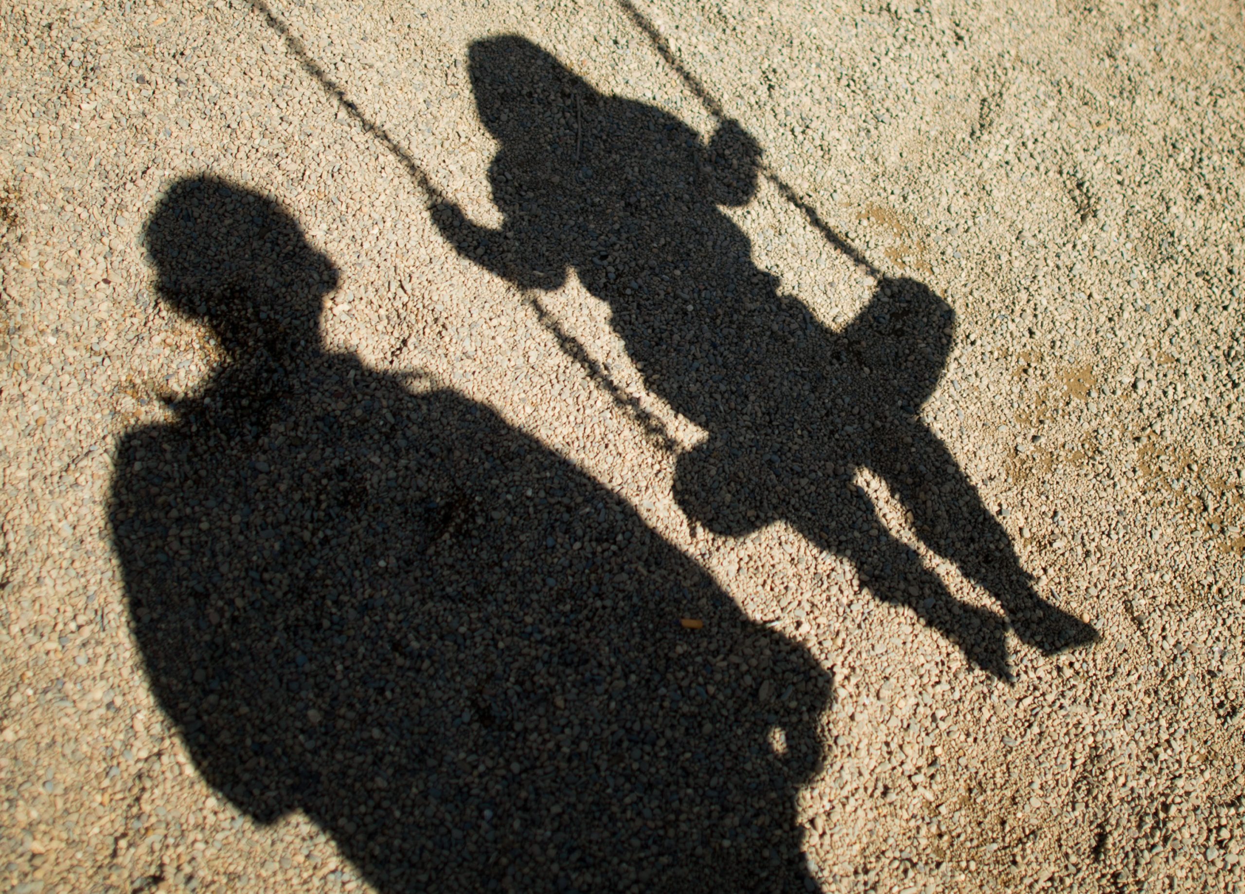 Schatten eines Mannes und eines Kindes auf einer Schaukel