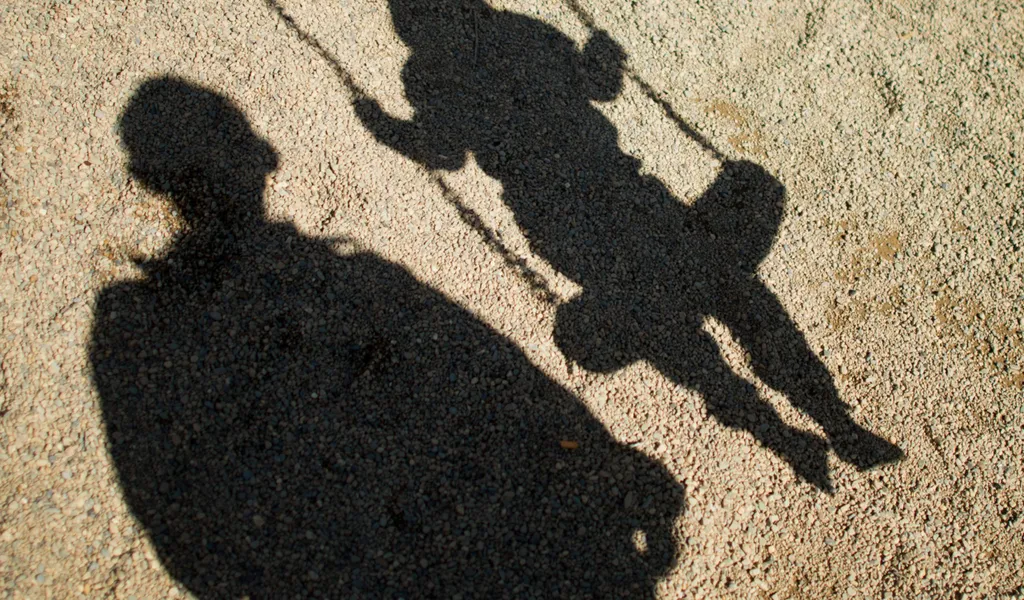 Schatten eines Mannes und eines Kindes auf einer Schaukel