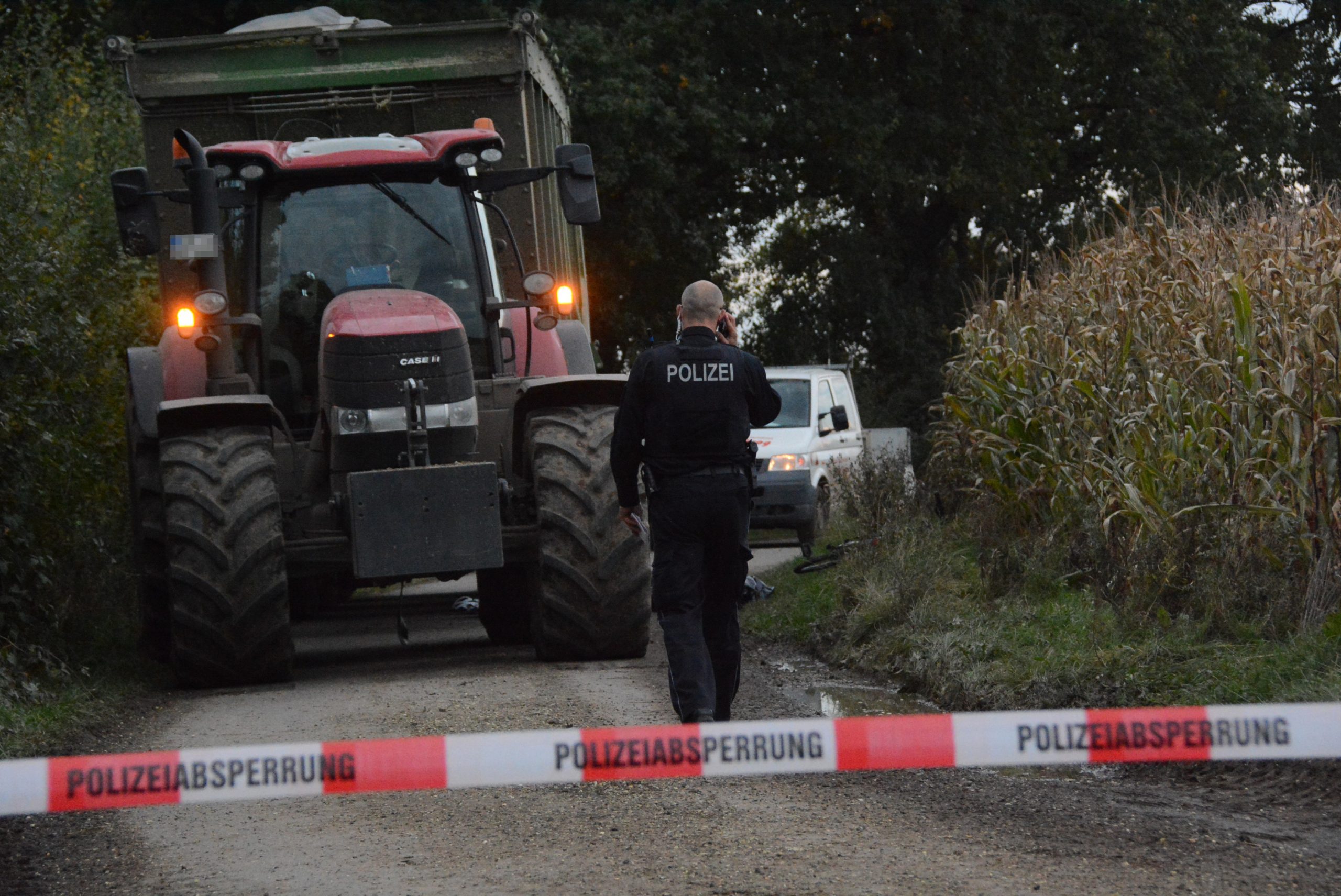 Ein Traktor mit Anhänger steht auf einem Feldweg, davor ein Polizist