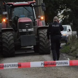 Ein Traktor mit Anhänger steht auf einem Feldweg, davor ein Polizist