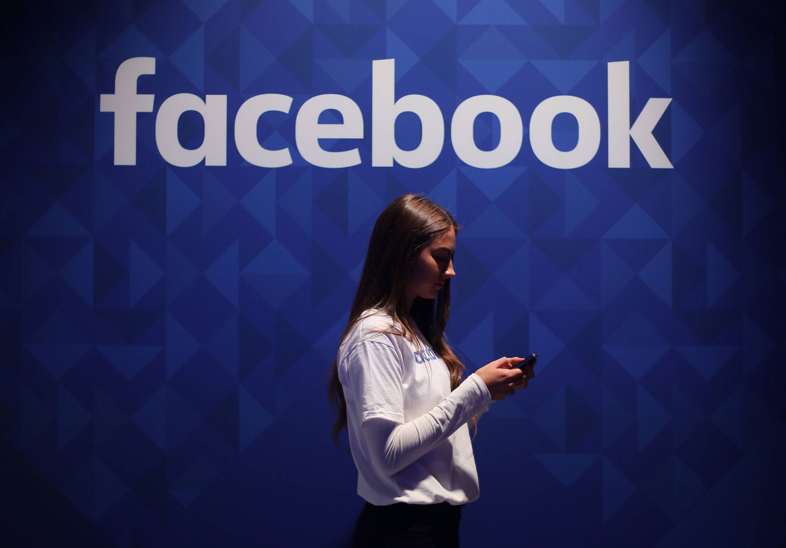 Eine Frau steht vor einem Facebook-Logo (Symbolbild).