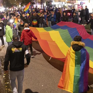 Menschen stehen mit einer großen Regenbogenflagge in der Hand auf einer Demo