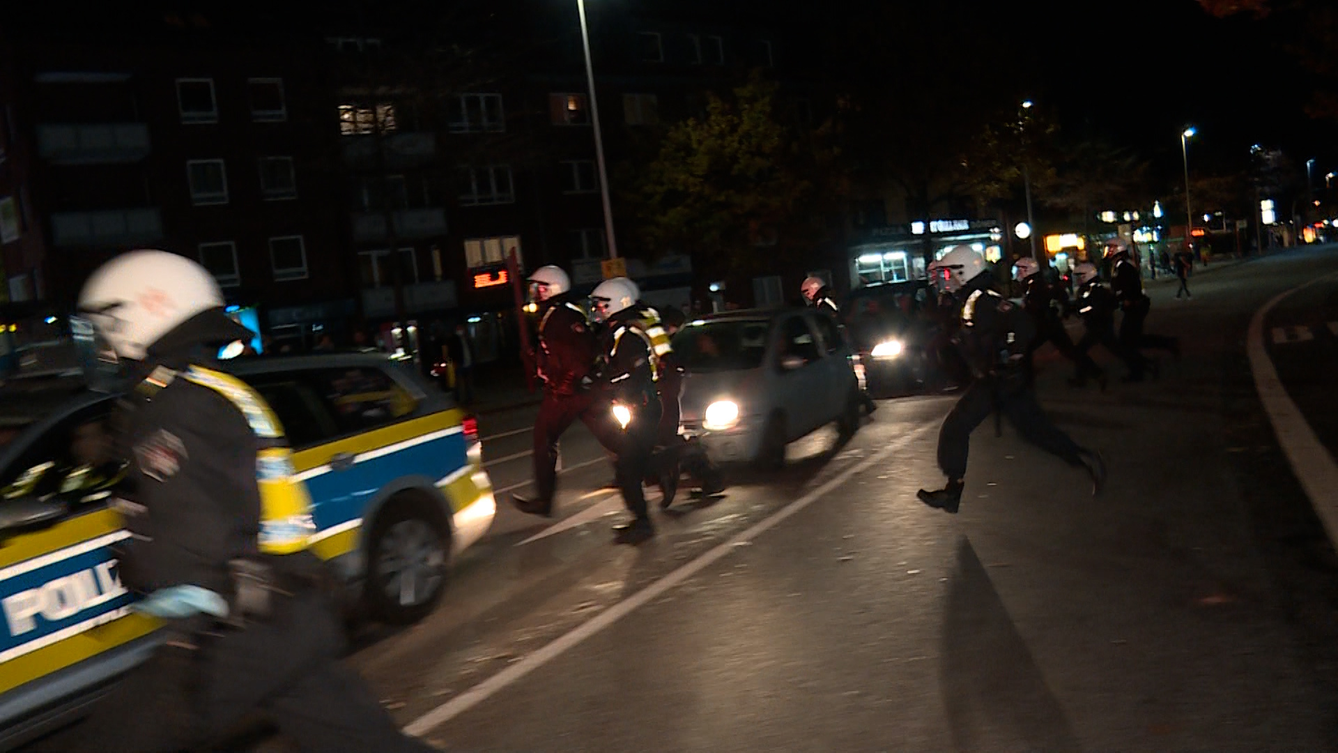 Polizisten laufen mit Helmen geschützt über eine Straße