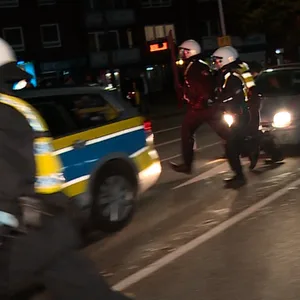 Polizisten laufen mit Helmen geschützt über eine Straße