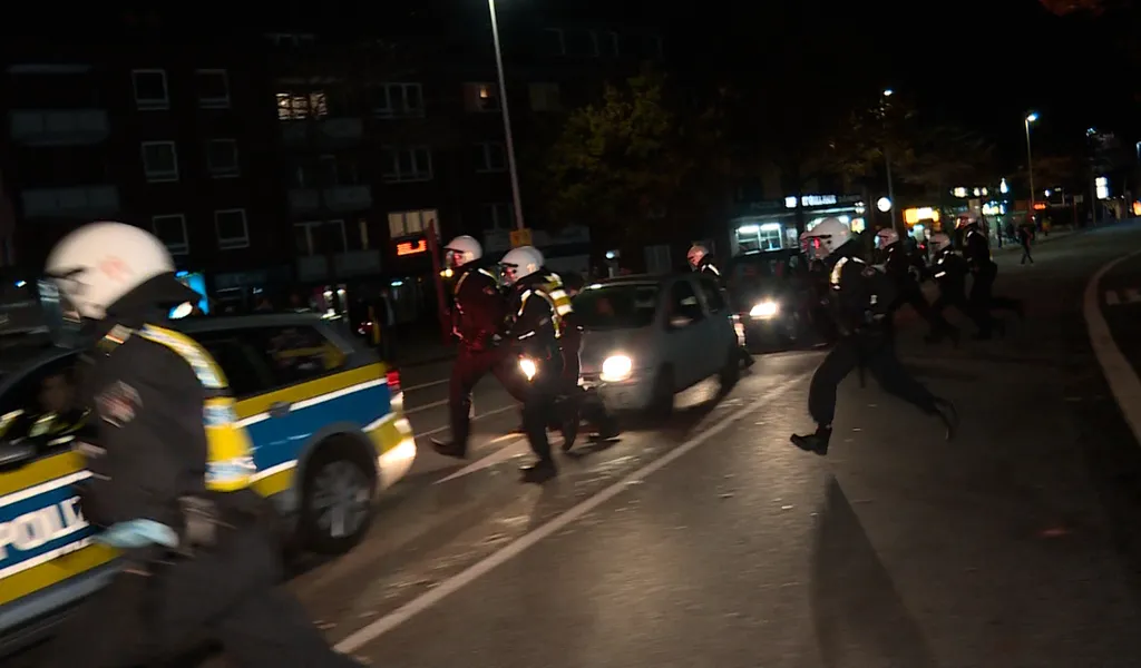 Polizisten laufen mit Helmen geschützt über eine Straße