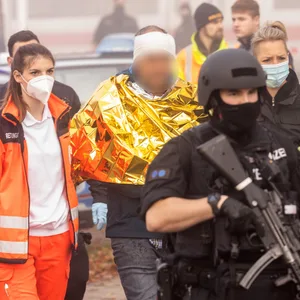 Eine festgenommene männliche Person wird am Bahnhof von Polizei und Rettungskräften weggeführt.