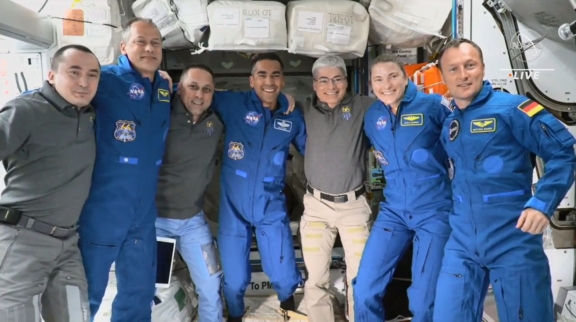 Sieben Personen posieren Arm in Arm für ein Foto auf der Internationalen Raumstation ISS