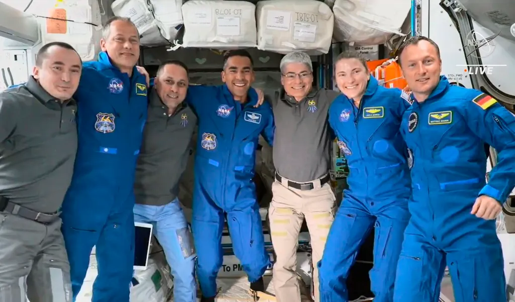 Sieben Personen posieren Arm in Arm für ein Foto auf der Internationalen Raumstation ISS