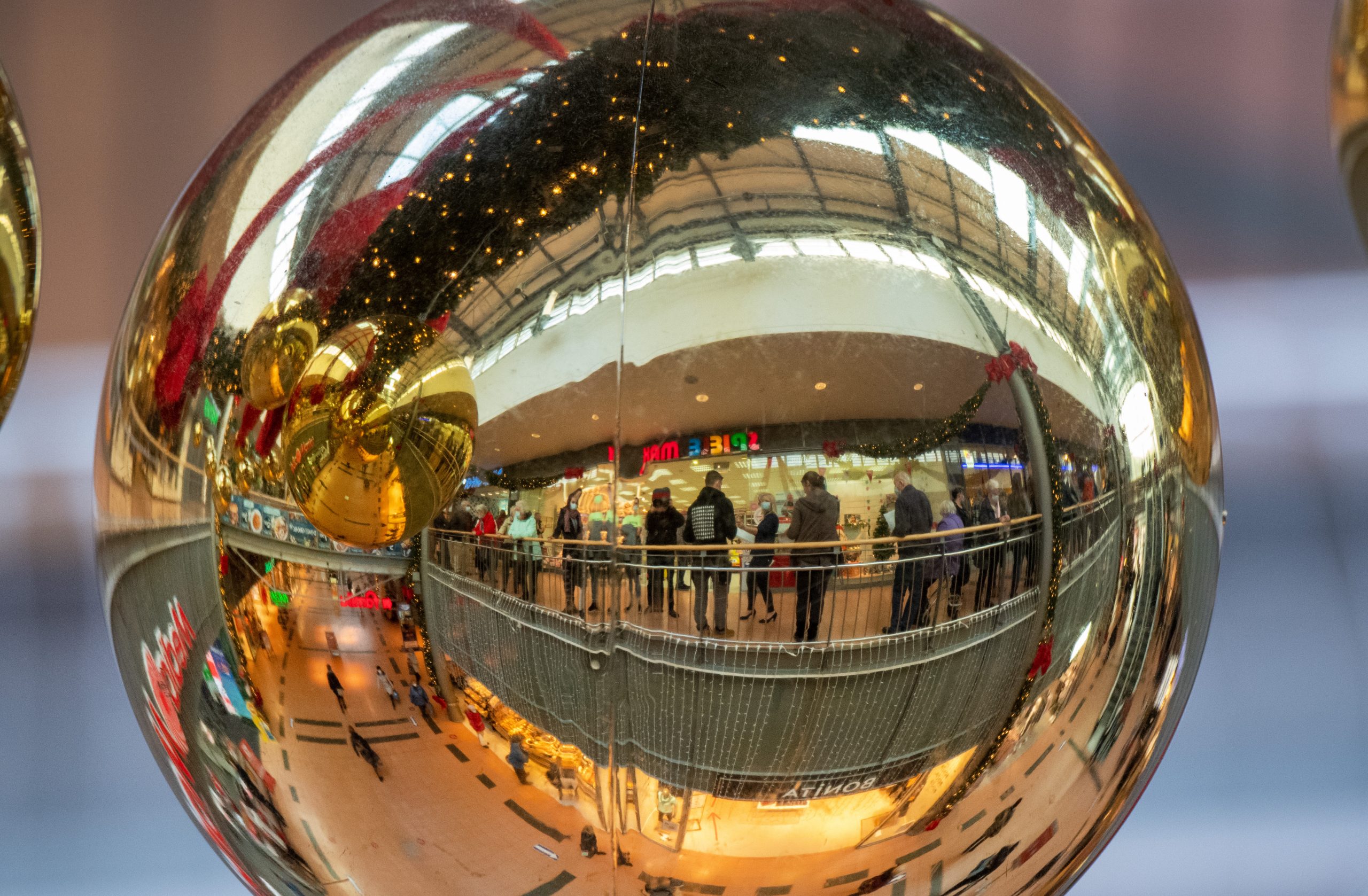 Die Innenansicht des Einkaufszentrum Strelapark mit eine Schlange von Impflingen spiegelt sich in einer Weihnachtskugel