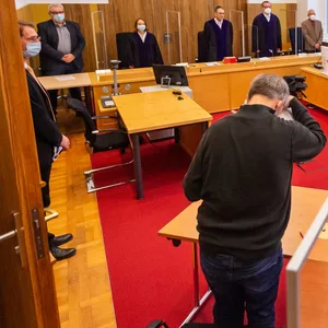 Der Kläger (Mittig) sitzt vor Prozessbeginn im Saal vom Landessozialgericht Niedersachsen-Bremen.
