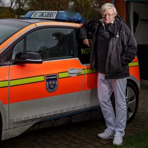 Rolf-Ferdinand Gehre, Inselarzt auf Pellworm, steht neben seiner Praxis am Notarztwagen.