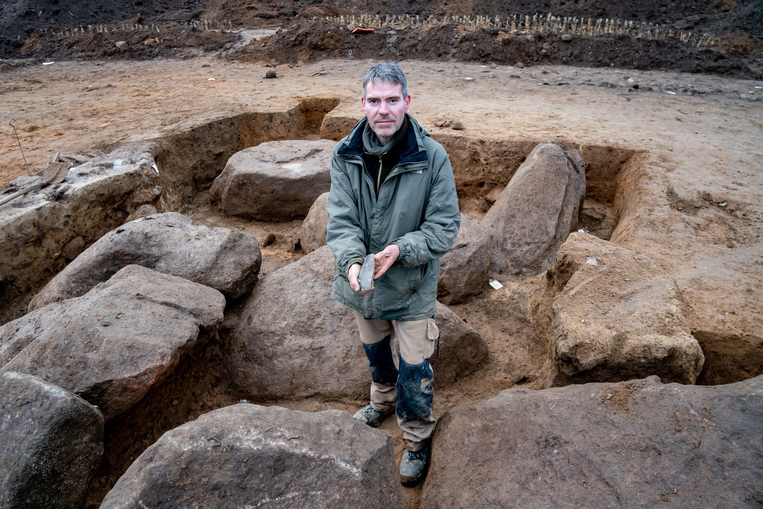 Ringo Klooß, Grabungsleiter, zeigt in der Ausgrabungsstelle eines Großsteingrabes aus der Trichterbecherzeit ein darin gefundenes Feuersteinbeil.