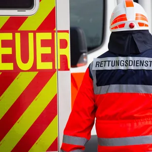 Ein Mitarbeiter des Rettungsdienstes trägt seine Sicherheitskleidung und steht neben einem Rettungswagen