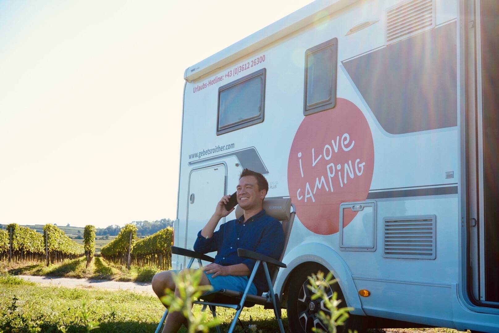 Ein Mann telefoniert in einem Campingstuhl vor einem Wohnmobil sitzend