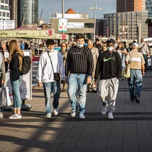 Menschen gehen an den Landungsbrücken in Hamburg bei Sonnenschein