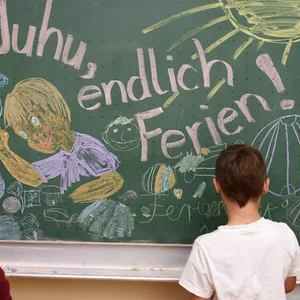 Erst- und Zweitklässler der Grundschule malen am letzten Schultag des Jahres für den Fotografen ein Bild an die Tafel, auf dem «Juhu, endlich Ferien», zu lesen ist.