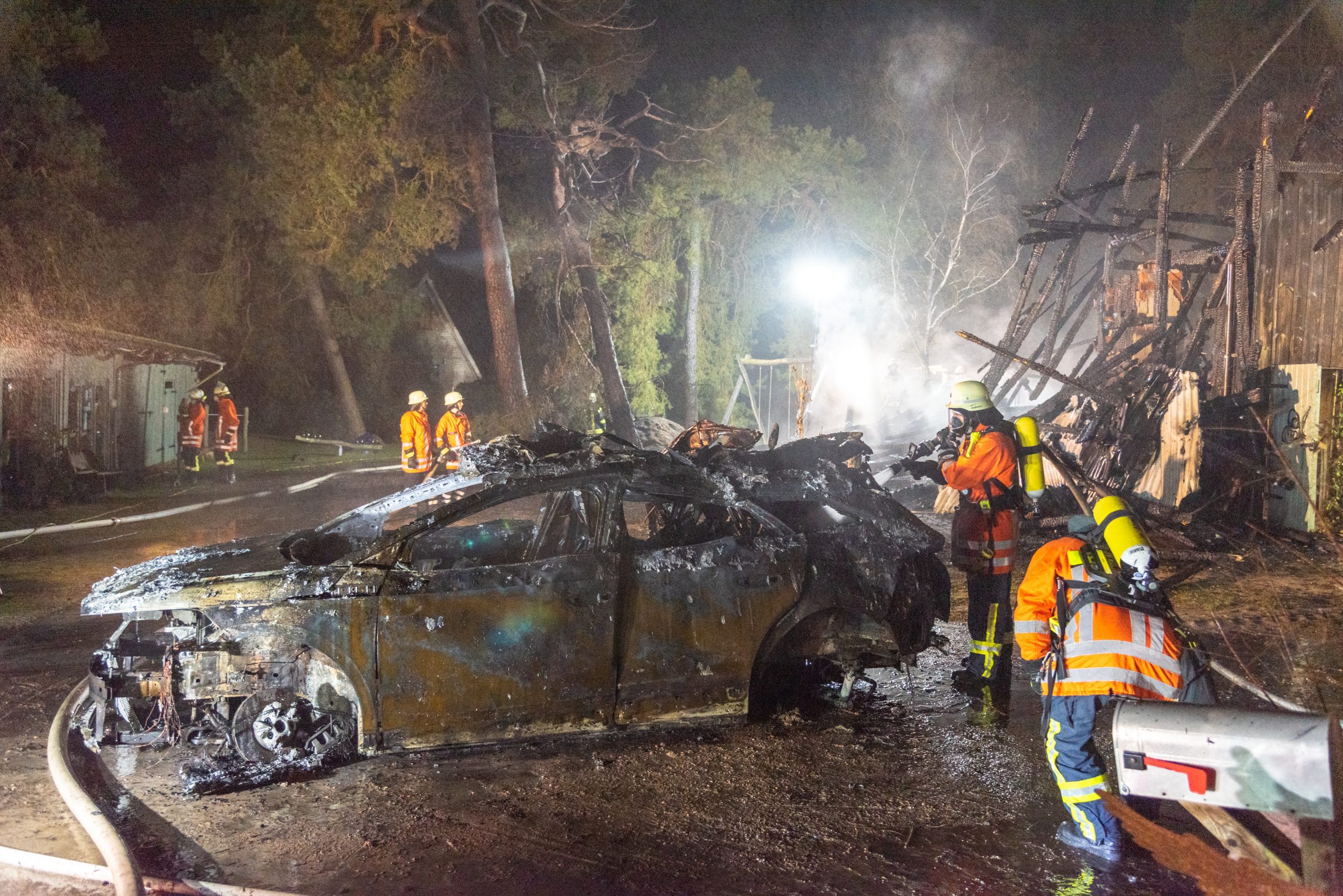 Feuerwehrleute löschen ein E-Auto nach einem Lagerhallenbrand in Ollsen.