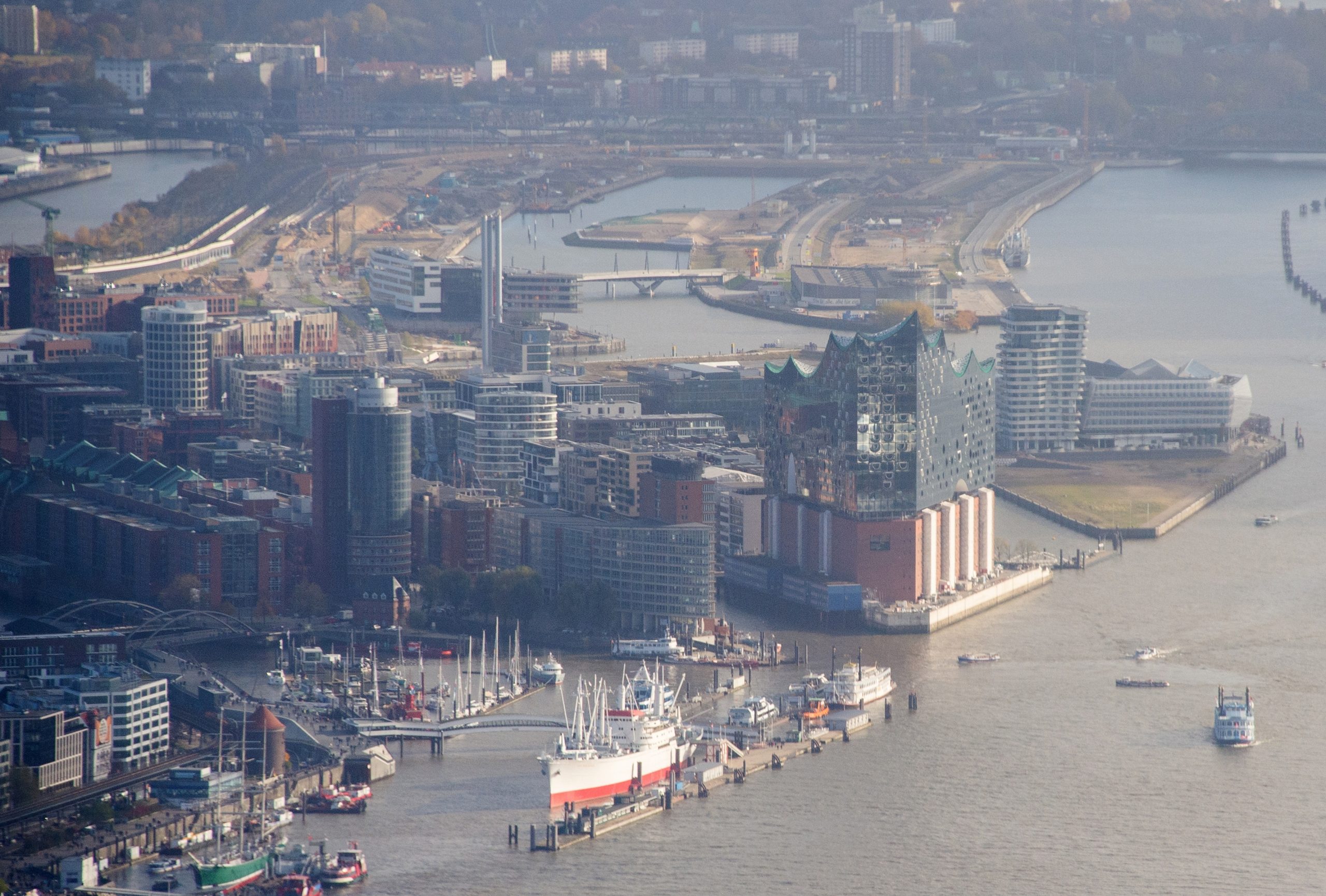 Blick auf den Hafen mit den Landungsbrücken (links), der Elbphilharmonie (Mitte) und dem Stadtteil HafenCity (oben).