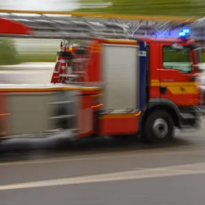 Ein Feuerwehrfahrzeug mit Drehleiter fährt in der Innenstadt zu einem Einsatz.