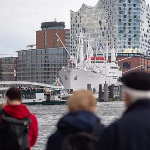 Passanten vor der Hafenkulisse mit Elbphilharmonie und Museumsschiff Cap San Diego auf den Landungsbrücken an der Elbe.