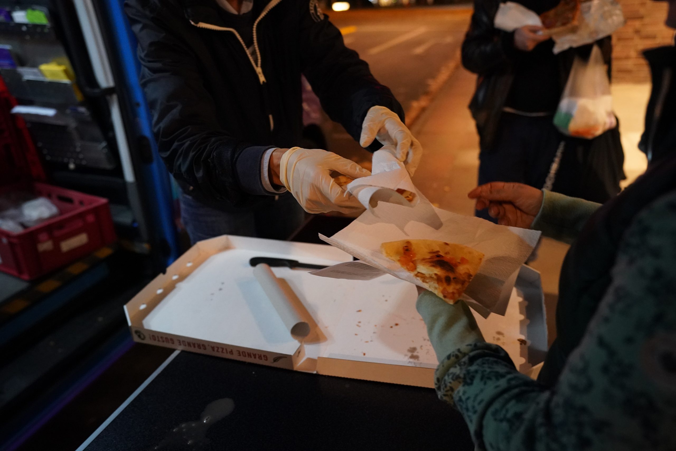 Eine ehrenamtliche Helferin des Mitternachstbusses für obdachlose Menschen, überreicht in der Innenstadt einer Frau ein Stück Pizza.