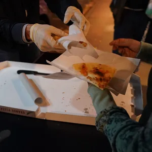 Eine ehrenamtliche Helferin des Mitternachstbusses für obdachlose Menschen, überreicht in der Innenstadt einer Frau ein Stück Pizza.