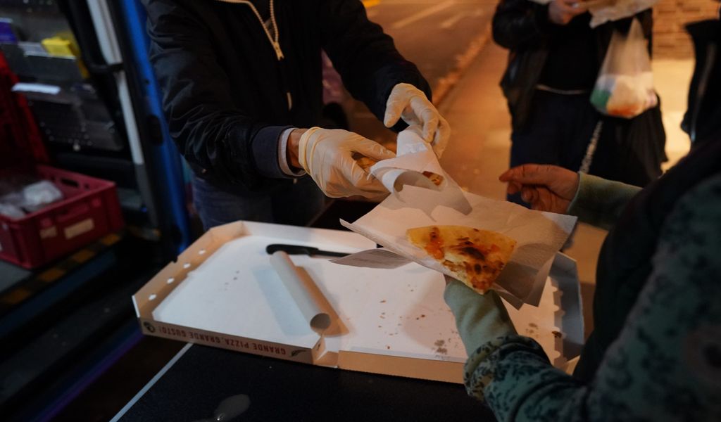 Eine ehrenamtliche Helferin des Mitternachstbusses für obdachlose Menschen, überreicht in der Innenstadt einer Frau ein Stück Pizza.
