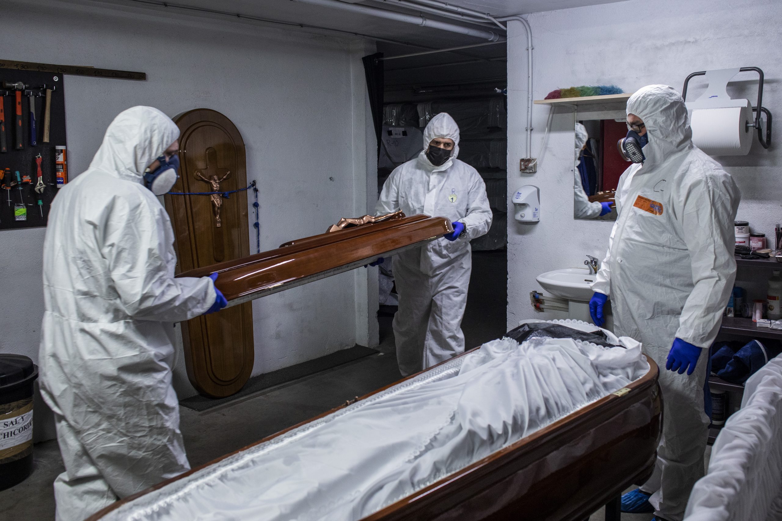 Mitarbeiter in Schutzausrüstung verschließen den Sarg eines Corona-Toten in einem Bestattungsunternehmen.