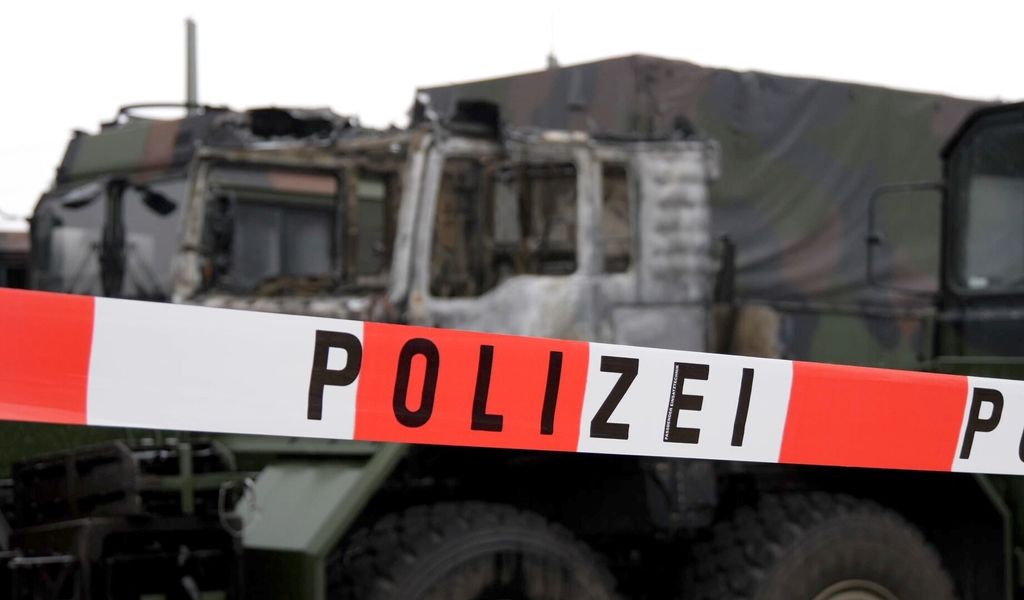 Die Zugmaschine eines Bundeswehrfahrzeuges steht ausgebrannt auf dem Gelände einer Nutzfahrzeugfirma hinter Absperrband der Polizei.