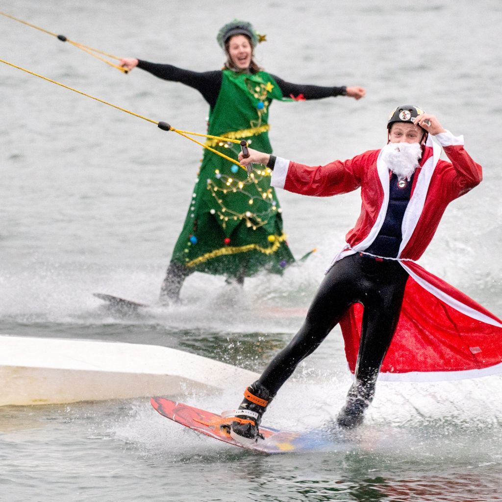 Die Teilnehmer Wilke (vorne) und Johann fahren, verkleidet als Weihnachtsmann und Tannenbaum, mit ihren Wakeboards über einen Badesee im Ortsteil Tannenhausen. 