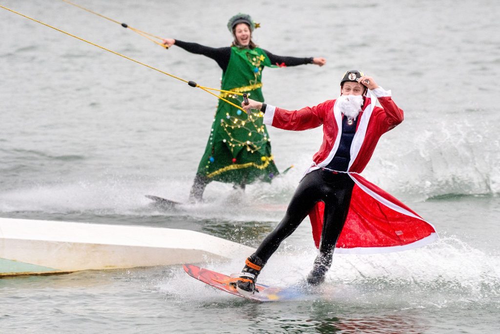 Die Teilnehmer Wilke (vorne) und Johann fahren, verkleidet als Weihnachtsmann und Tannenbaum, mit ihren Wakeboards über einen Badesee im Ortsteil Tannenhausen.