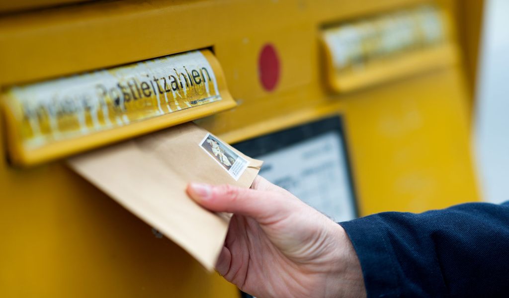 Ein Mann wirft einen Brief in einen Briefkasten.