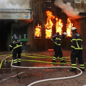 Feuerwehrkräfte legen Löschleitungen. Im Inneren des Clubhauses breiten sich Flammen aus.