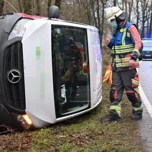 Einsatzkräfte der Feuerwehr neben dem umgekippten Transporter.