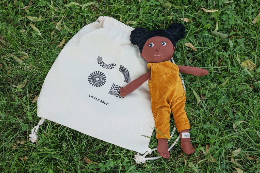 Die „Little Ashé“-Puppe „Taya“ neben einem einem Stoffbeutel, in dem die Puppen verpackt werden.
