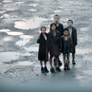 5 Kinder stehen mit KZ-Kleidung und kurzgeschorenen Haaren auf einem Platz voller Pfützen