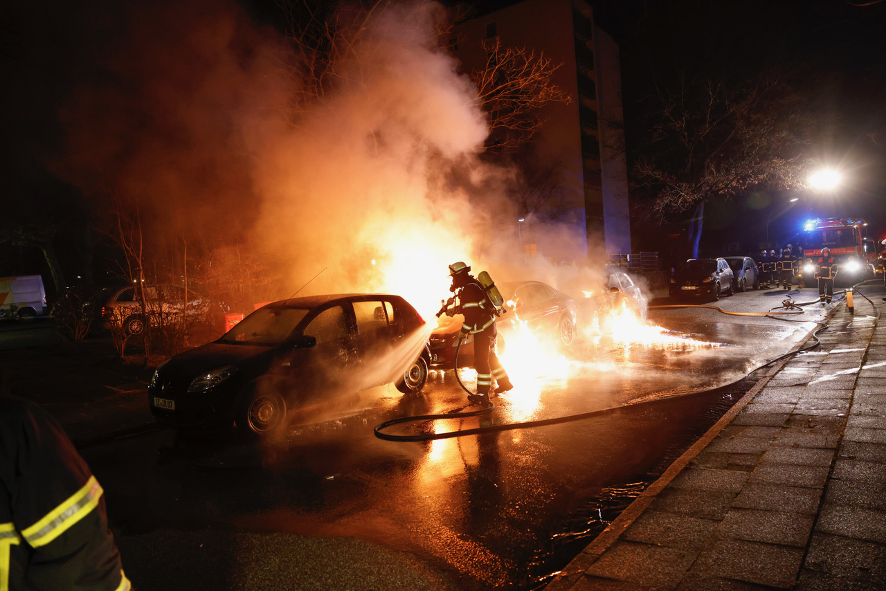 Ein Feuerwehrmann löscht ein brennendes Auto, Flammen ziehen die Straße entlang