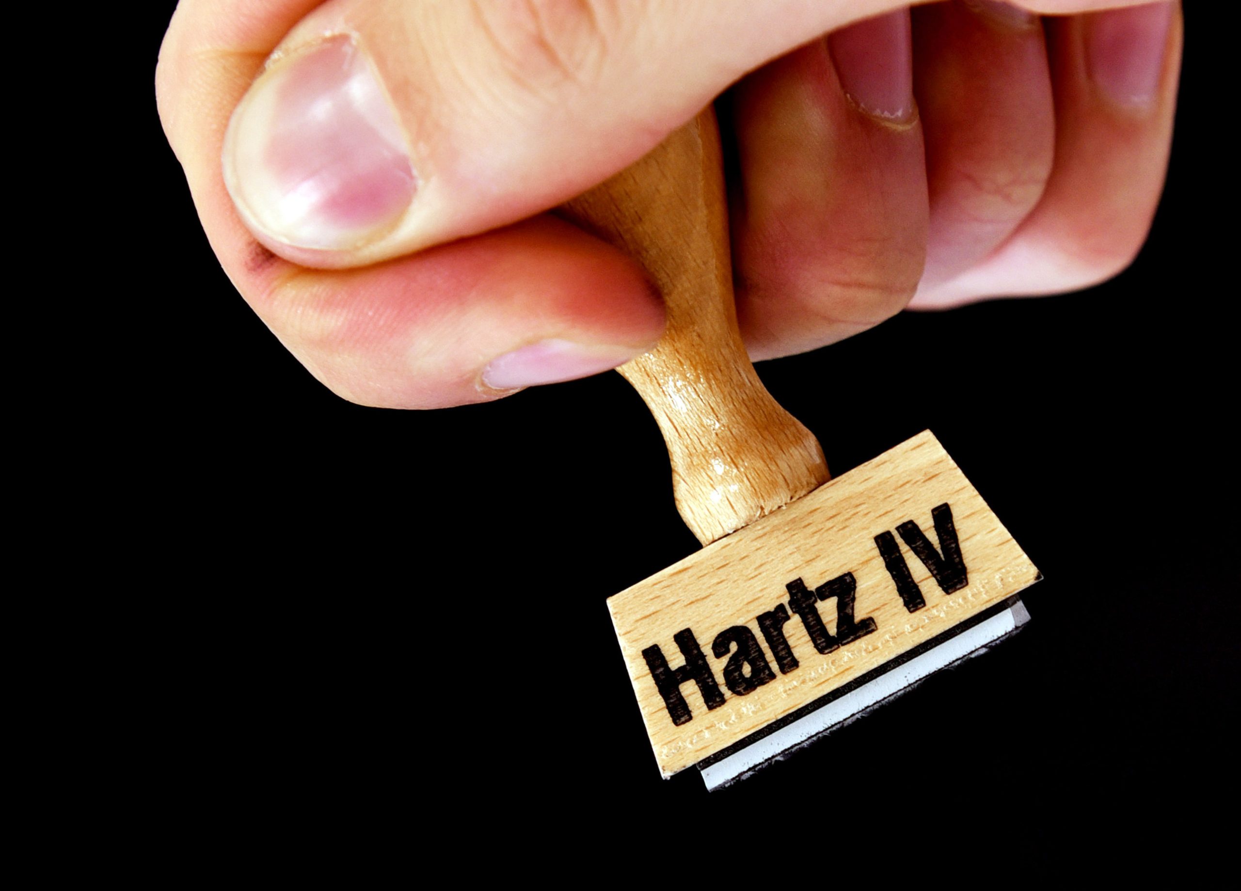 Eine Hand hält einen Stempel mit der Aufschrift „Hartz IV“.