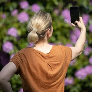 Eine Frau hält ein Smartphone in der Hand und macht ein Selfie.