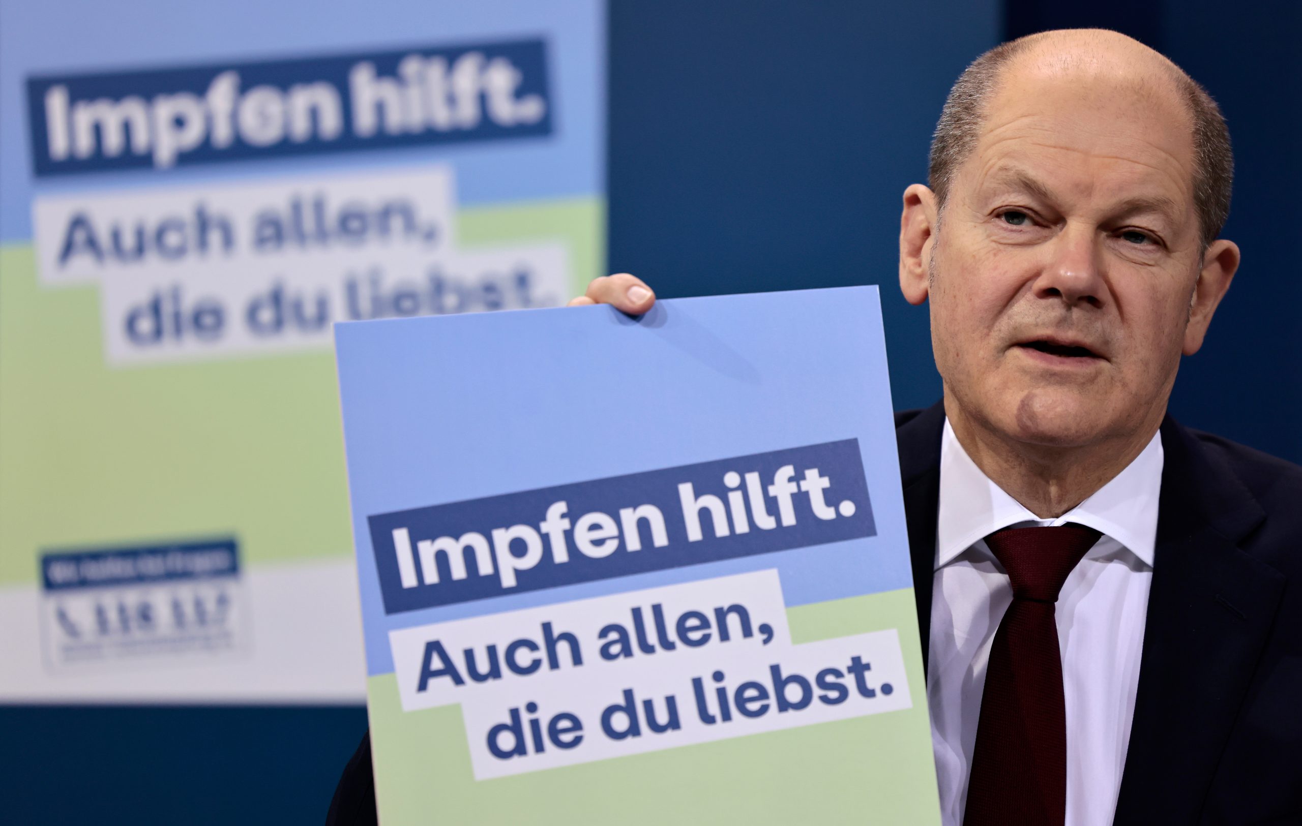 Bundeskanzler Olaf Scholz (SPD) präsentiert ein Plakat für eine neue Impfkampagne