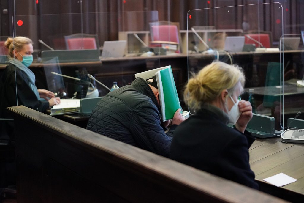 Der Angeklagte (M) hält sich zu Beginn des Prozesses einen Aktenordner im Sitzungssaal im Strafjustizgebäude vor das Gesicht.