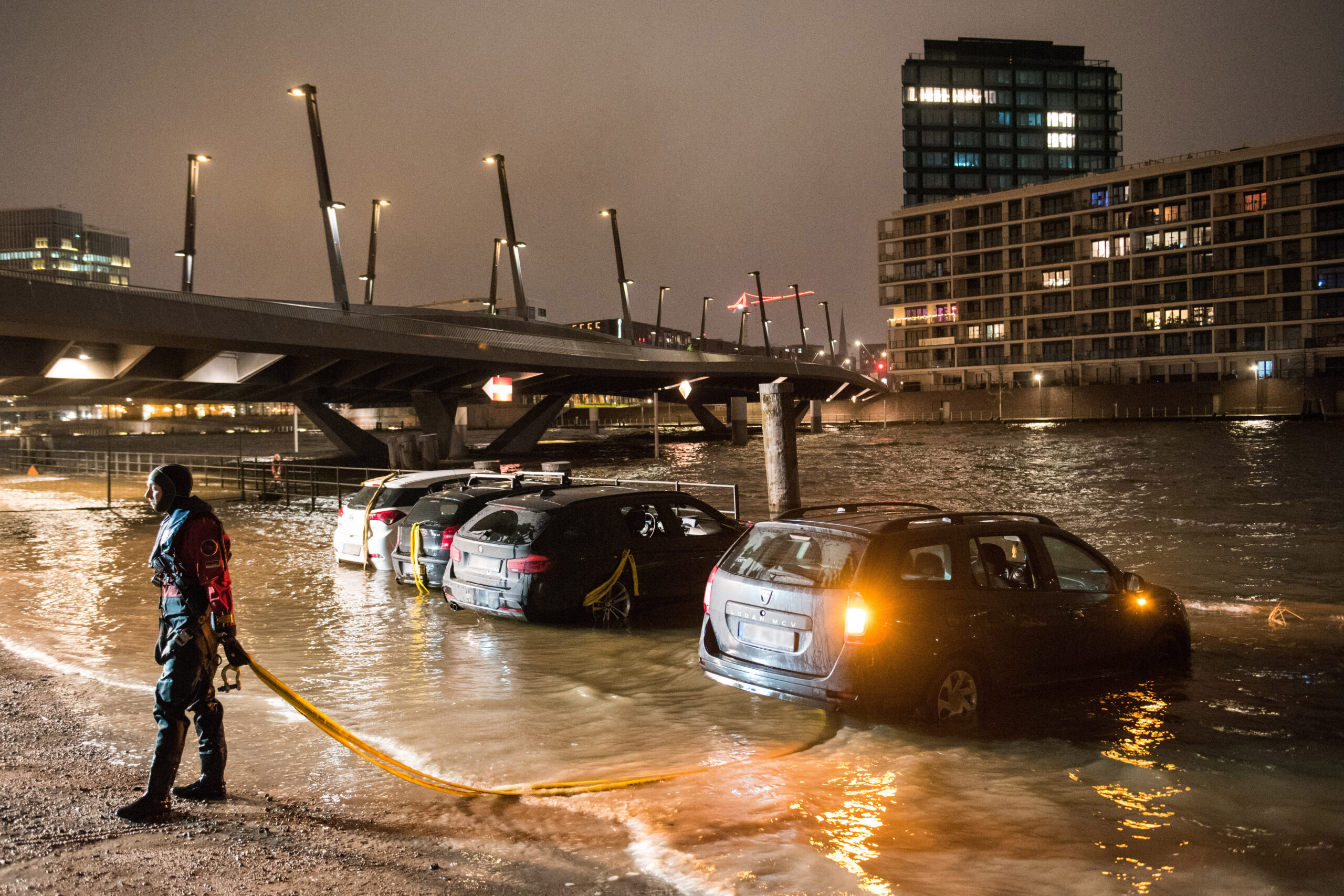 Autos stehen während einer Sturmflut im Wasser der Elbe auf einem Parkplatz in der HafenCity und werden von einem Feuerwehrmann gesichert.