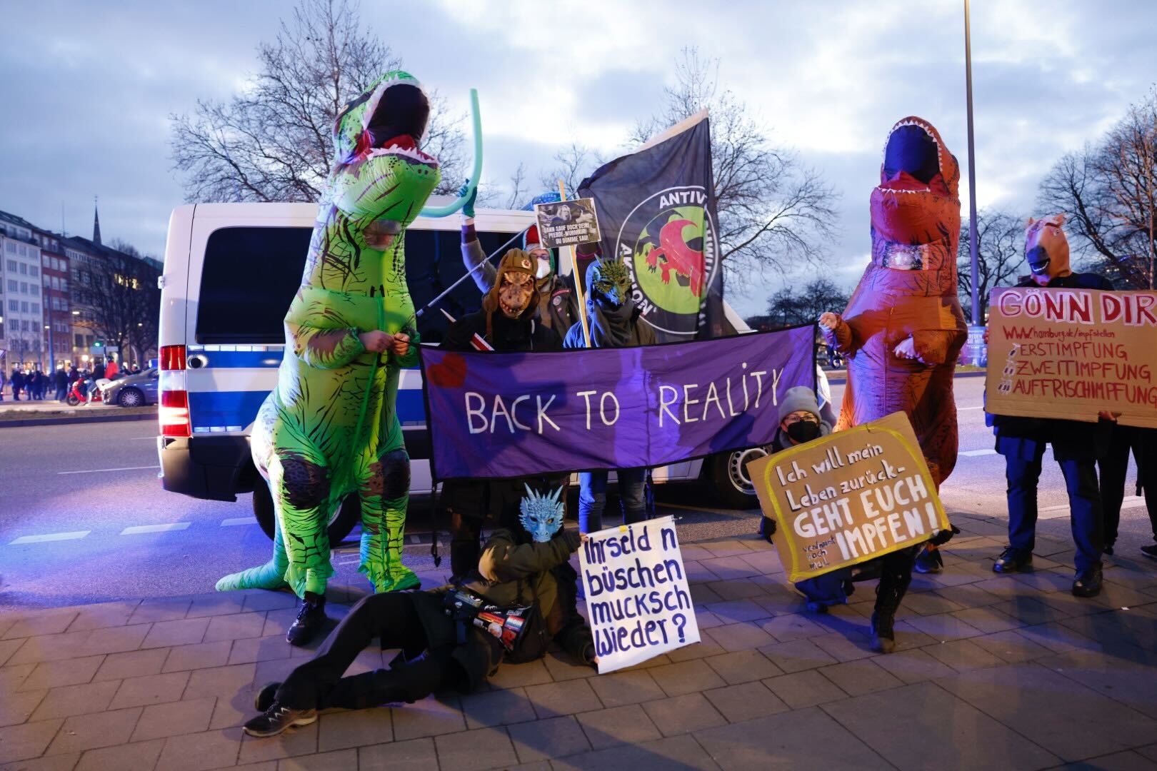 Demonstrierende in Dinosaurier-Kostümen posieren mit Schildern wir "Back to reality"