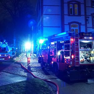 Feuerwehrfahrzeuge stehen vor einem Haus, Blaulicht leuchtet