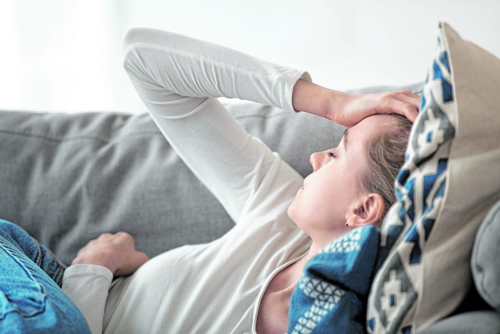 Eine junge Frau liegt mit Kopfschmerzen auf dem Sofa.