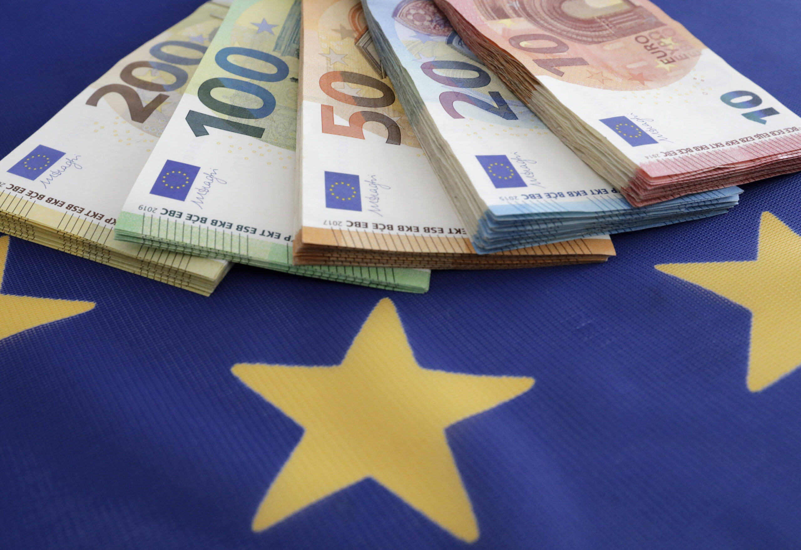 Symbolfoto: Euroscheine verschiedener Stückelungen liegen auf einer Europafahne.
