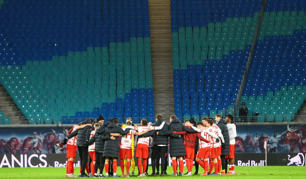 Spieler und Trainer von Rb-Leipzig bilden einen Mannschaftskreis vor leerer Tribüne.