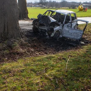 Ein ausgebranntes Auto steht im Straßengraben vor einem Baum